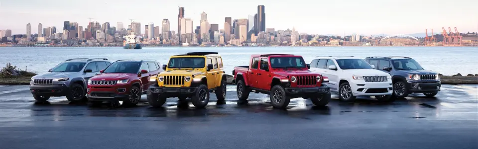 Five Jeeps (red, blue, white, gray, black) parked in a snowy landscape with mountains in the background.