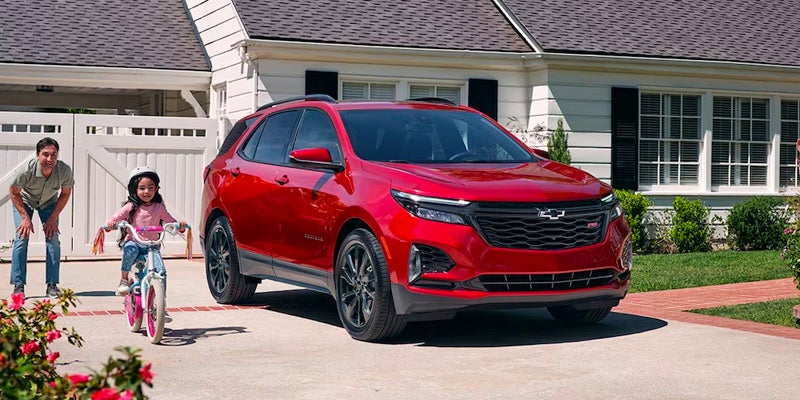 A red Chevrolet Equinox parked in a driveway beside a child cycling.