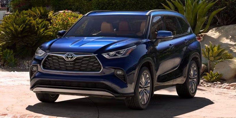 A blue Toyota Highlander SUV parked in a driveway with lush greenery