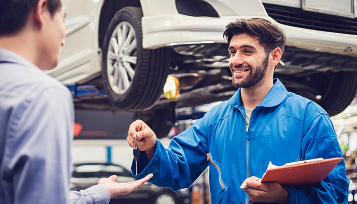 A smiling mechanic handing car keys to a customer in a garage.
